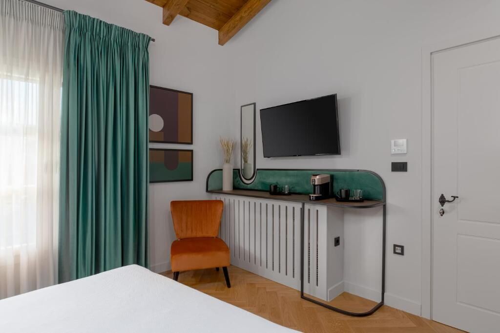 A modern room with a bed, a chair, a radiator, a TV, and a door.