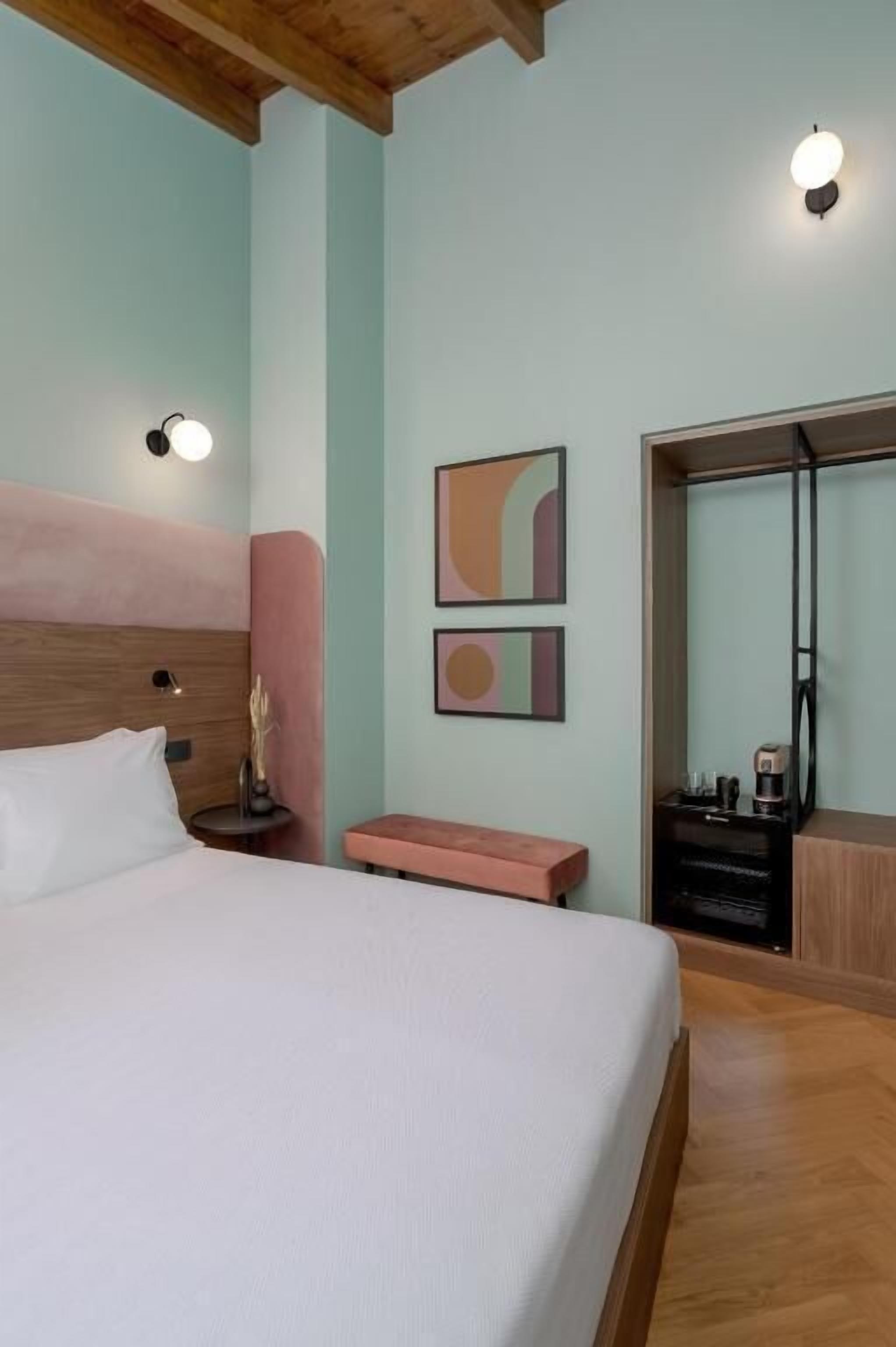 A bedroom with a bed, a bedside table, a bench, a mirror, and abstract wall art.