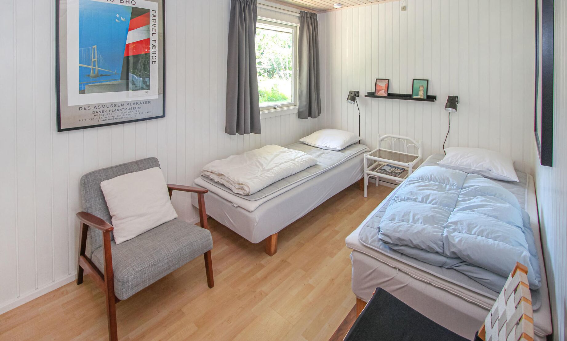 A small, well-lit room with two beds, a chair, and a window with curtains.