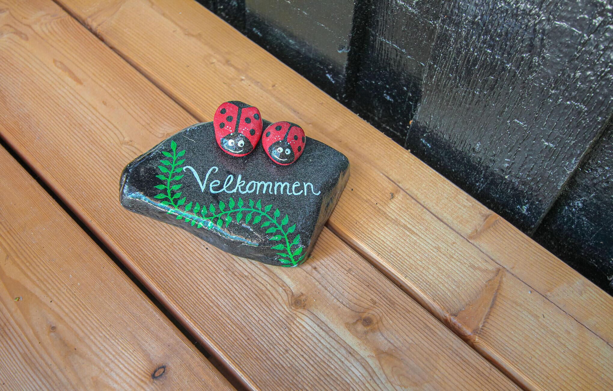 A wooden bench with a carved rock featuring a ladybug and the word "Velkommen" (Welcome).