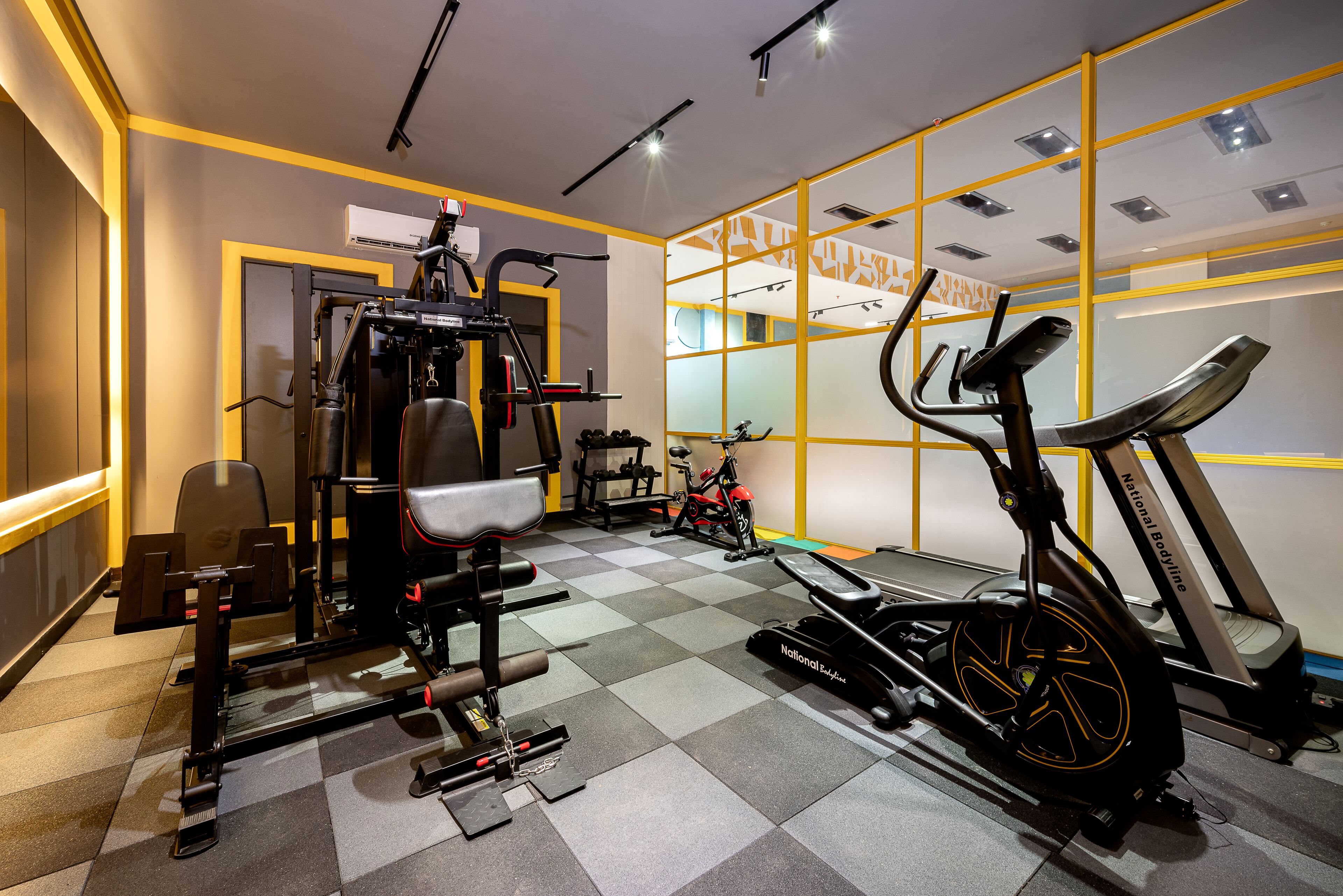 Une salle de sport équipée de divers appareils d’exercice, notamment un tapis de course, un vélo d’appartement et des appareils de musculation.