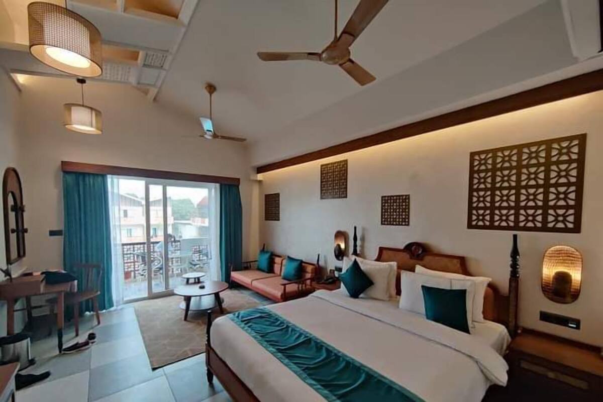 Quarto de hotel com cama, sofá, escrivaninha e varanda com vista.