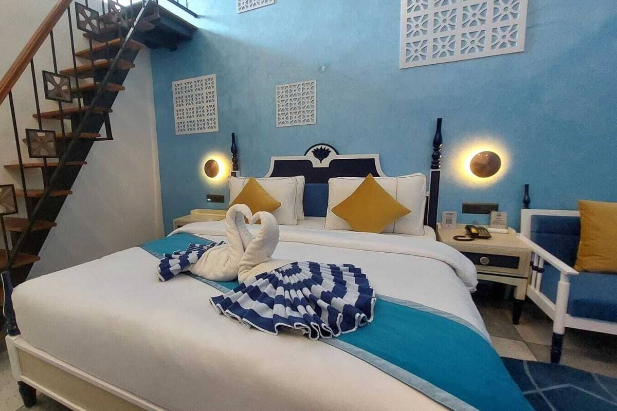 Quarto com cama, mesa de cabeceira, cadeira, escada e painéis decorativos na parede.