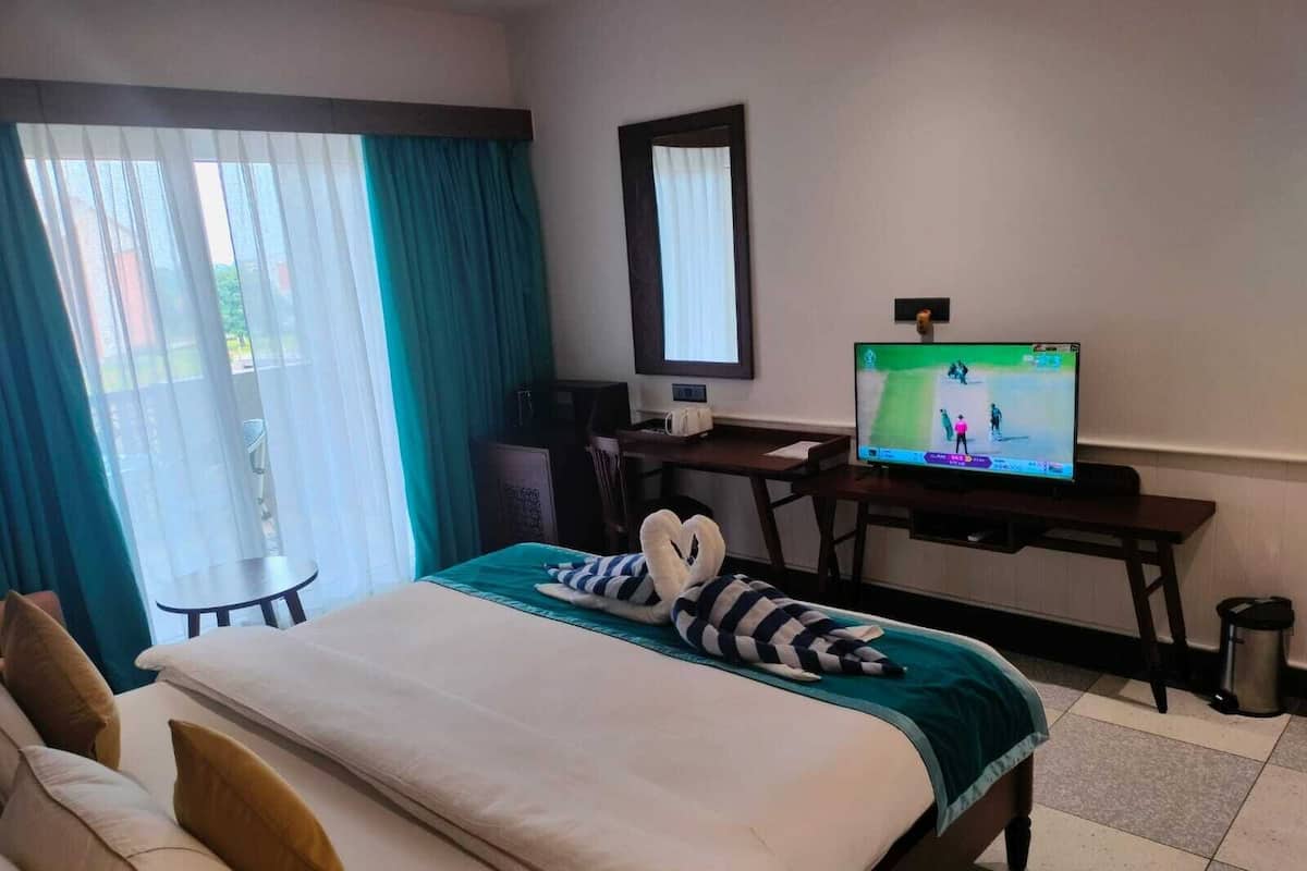 Quarto de hotel com cama, escrivaninha, televisão e vista para o exterior pela janela.