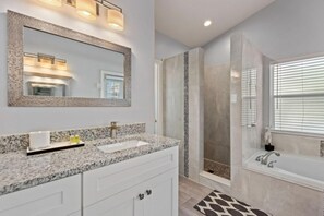 A modern bathroom with a granite countertop, a large mirror, a shower enclosure, and a bathtub. - Gilded Turtle by Shine Villas at Indian Creek (Kissimmee)