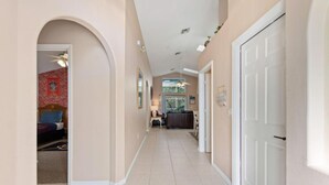 A hallway with a ceiling fan, a door on the right, and a room with a bed and a red wall in the background.