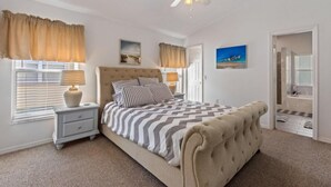 A bedroom with a large bed, a nightstand, a ceiling fan, and a door leading to a bathroom.
