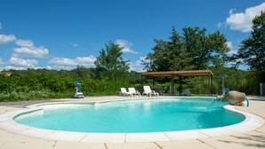 Piscina con bordo in legno e lettini da relax, circondata da vegetazione e alberi.