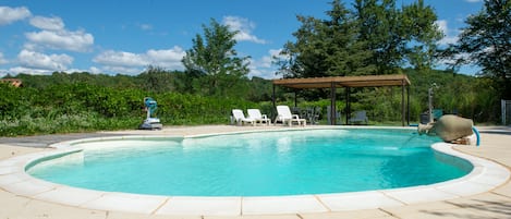 Una piscina con muelle de madera y sillones de descanso, rodeada de vegetación y árboles.