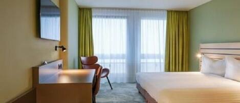 Habitación de hotel con cama, escritorio, silla y televisor en la pared.