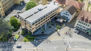 An aerial view of a hotel with a modern design, featuring a central courtyard, multiple parking spaces, and a surrounding urban environment. - flexy.motel Schönenwerd (Schonenwerd)