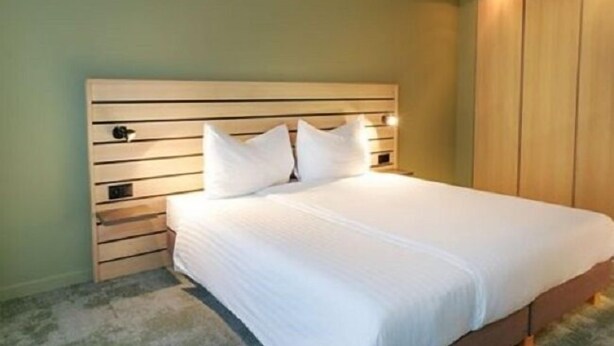 A neatly made bed with a wooden headboard and two pillows, a wooden nightstand, and a wardrobe with a mirror. - flexy.motel Schönenwerd (Schonenwerd)