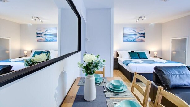 A modern hotel room with two beds, a dining area with a vase of flowers, and artwork on the walls. - Statera Apartments - Studio Apartment in Walworth (London)