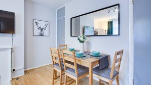 A dining area with a wooden table, four chairs, a TV, and a framed deer picture on the wall. - Statera Apartments - Studio Apartment in Walworth (London)
