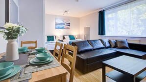 A modern room with a dining table set with green plates, a sofa with blue cushions, and a painting on the wall. - Statera Apartments - Studio Apartment in Walworth (London)