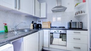 A modern kitchen with white cabinets, a stainless steel sink, a built-in oven, and a microwave. - Statera Apartments - Studio Apartment in Walworth (London)