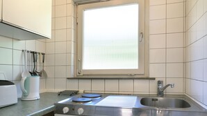 Une cuisine de taille réduite avec des meubles blancs, un évier en acier inoxydable et une fenêtre au-dessus du plan de travail.