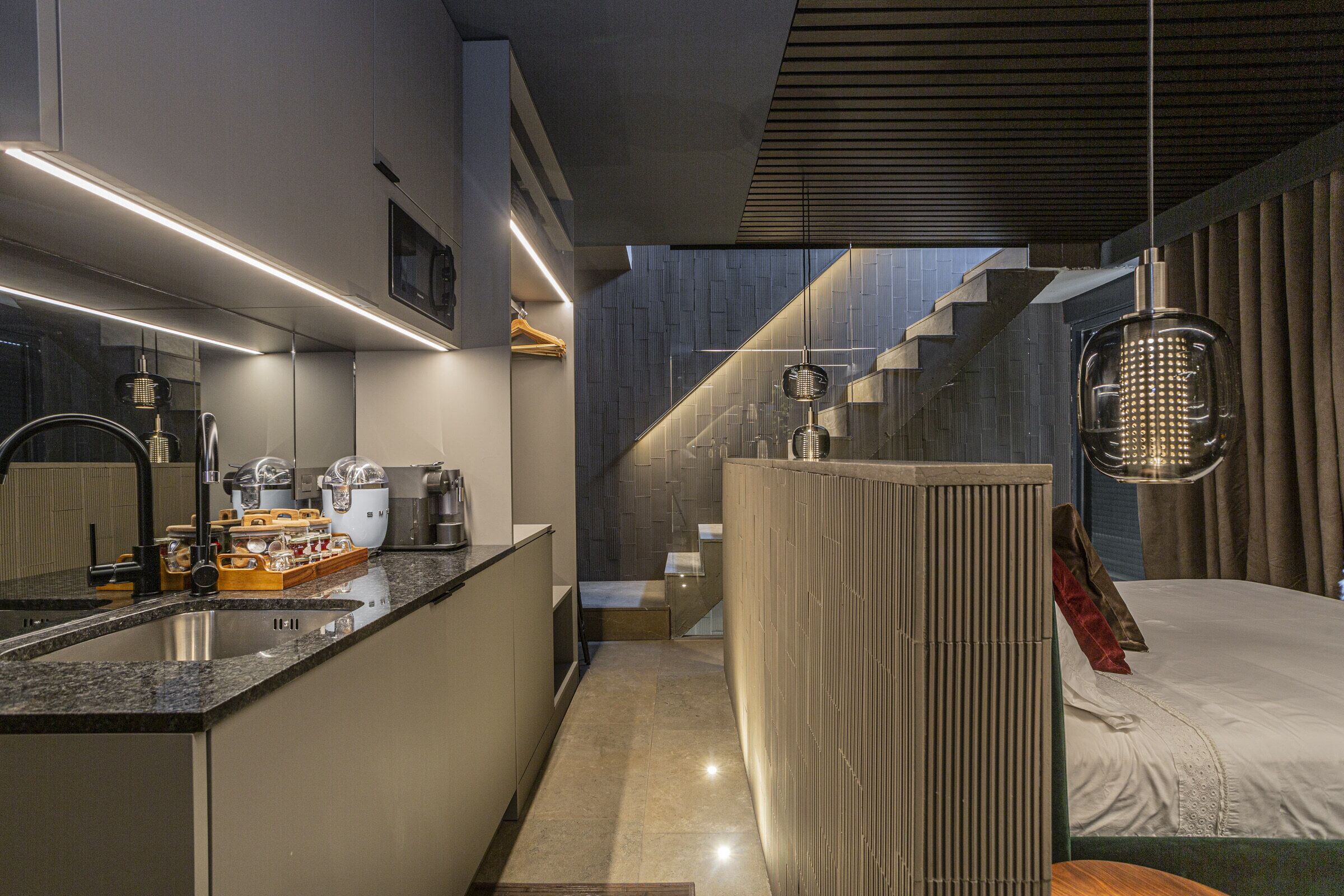 Una cocina moderna con una isla integrada, una escalera que conduce a un dormitorio y una lámpara colgante.