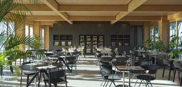 Un restaurante espacioso con varias mesas y sillas, una zona de bar y amplios ventanales que dejan entrar luz natural.