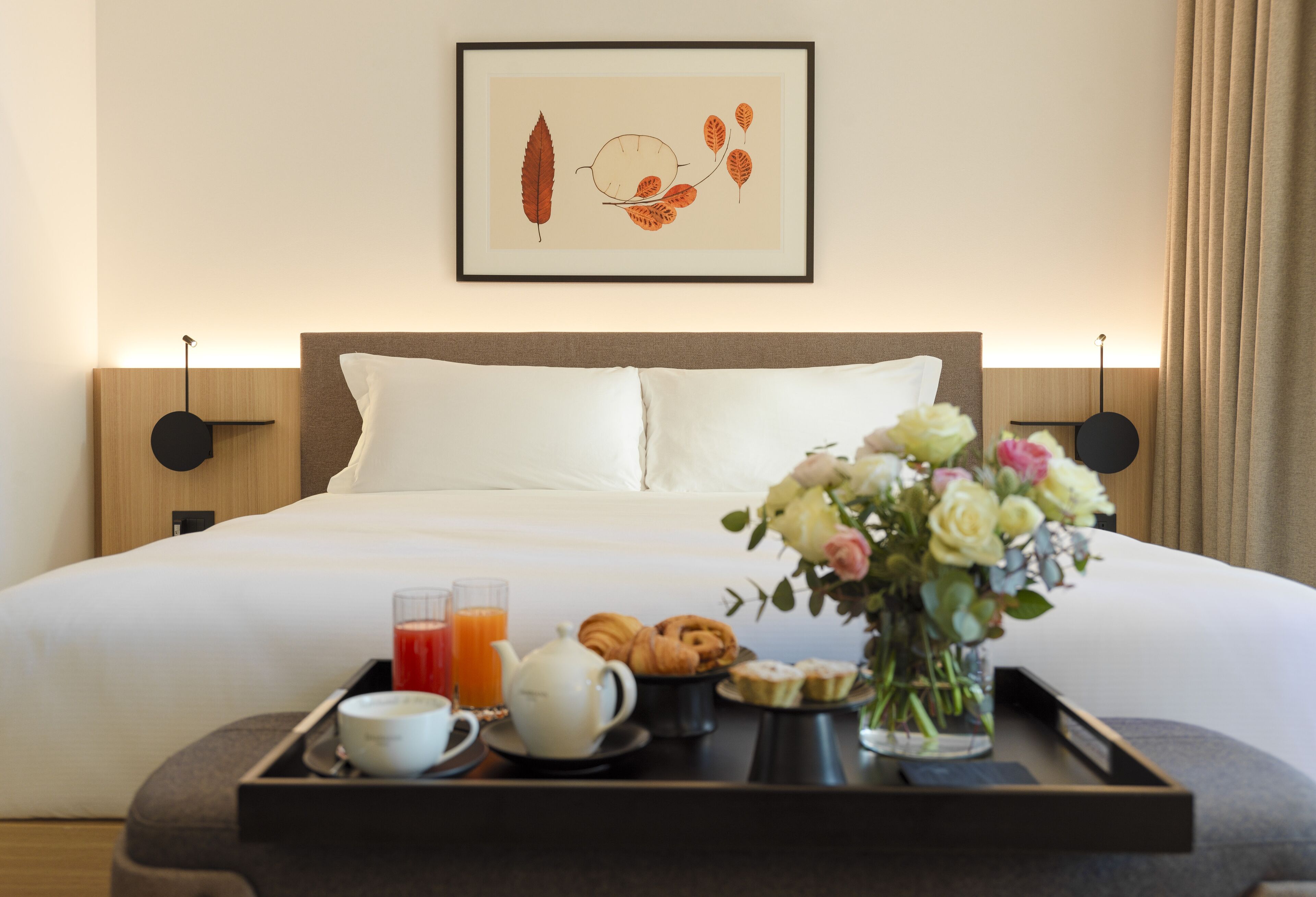 A neatly made bed with white linens, a tray with breakfast items, and a framed artwork above the bed.