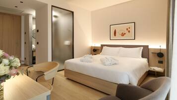 Ein modernes Hotelzimmer mit einem ordentlich bezogenen Bett, einem Schreibtisch mit Stuhl und einem Nachttisch mit Lampe.
