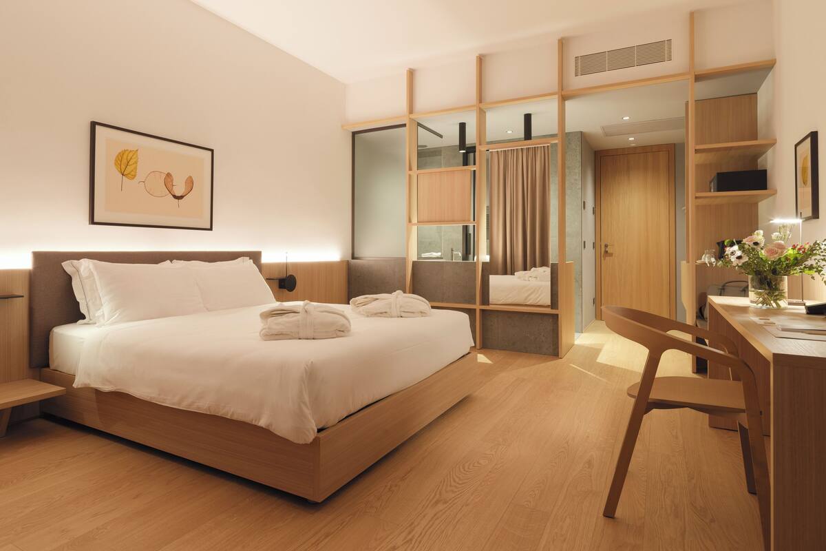 A modern hotel room with a wooden bed, bedside tables, a desk, and a mirror.