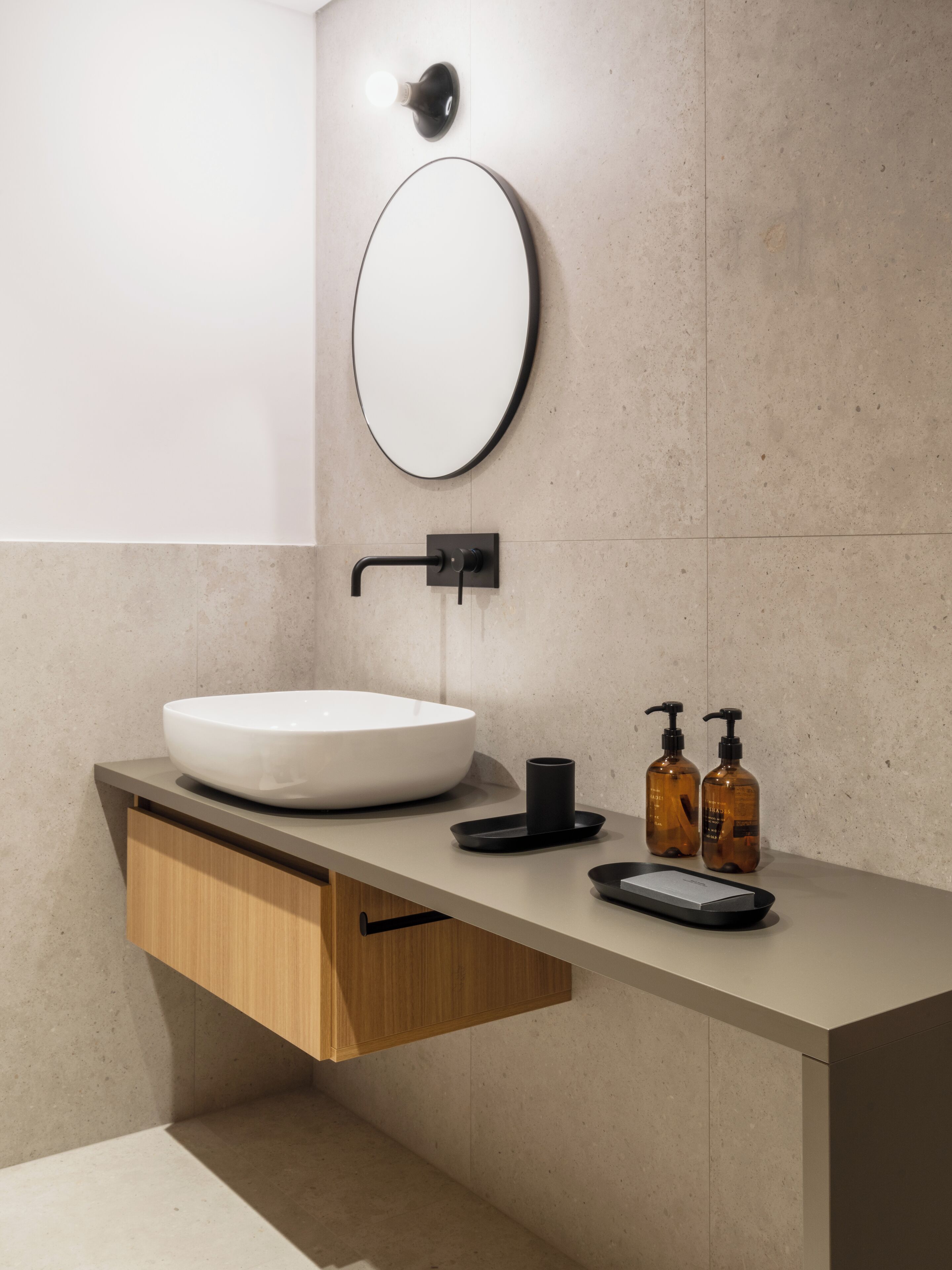 A modern bathroom with a round mirror, a white sink, and two soap dispensers.