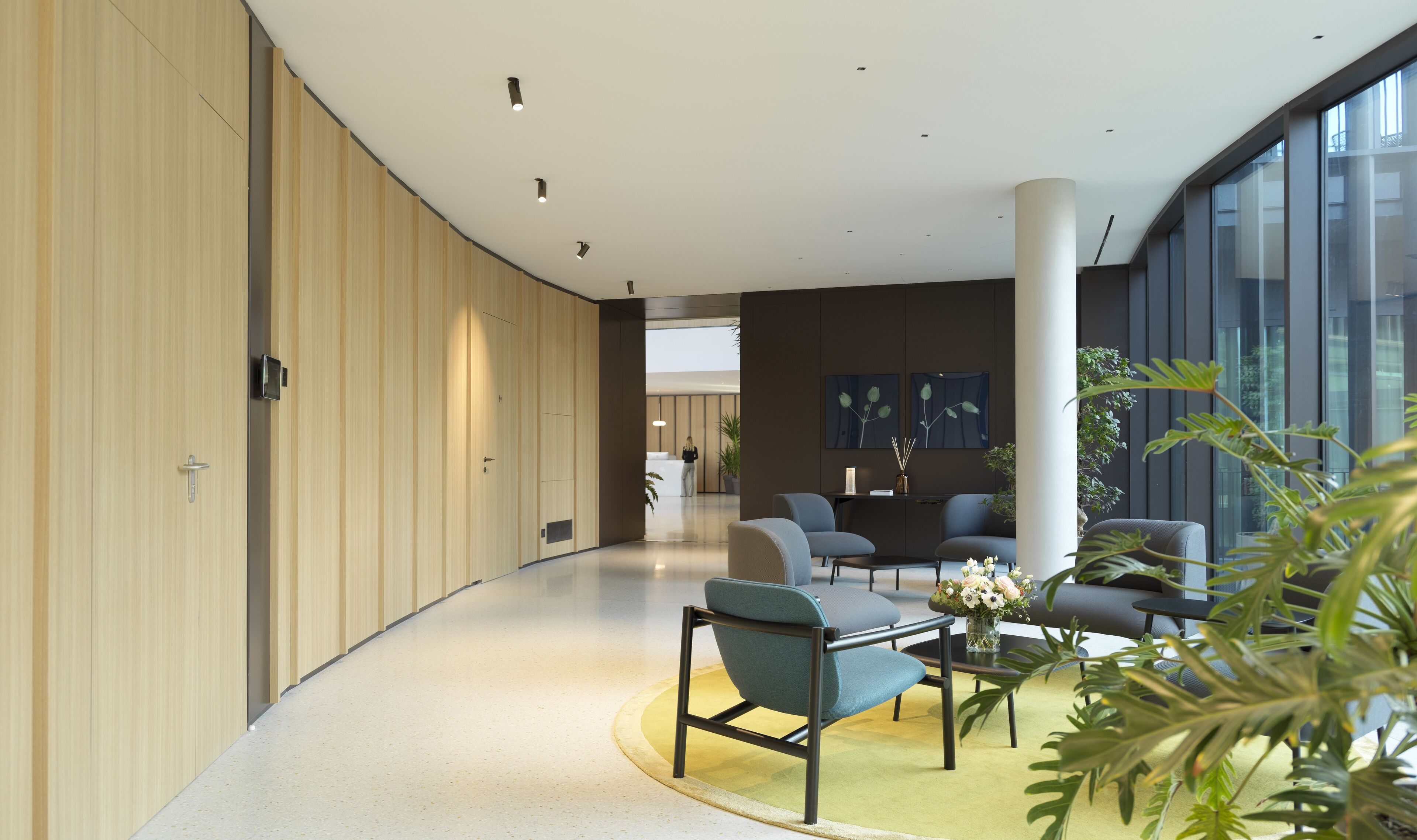 A modern interior with a curved wooden wall, a reception desk, seating area with chairs, and large windows.