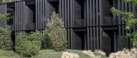 Un edificio moderno con fachada oscura, listones verticales y un balcón.