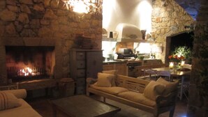 Una sala de estar acogedora con chimenea de piedra, asientos cómodos y un área de cocina visible a través de un arco.