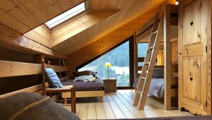 Un dormitorio acogedor en el ático, con techo inclinado, vigas de madera y un ventanal con vistas al exterior.