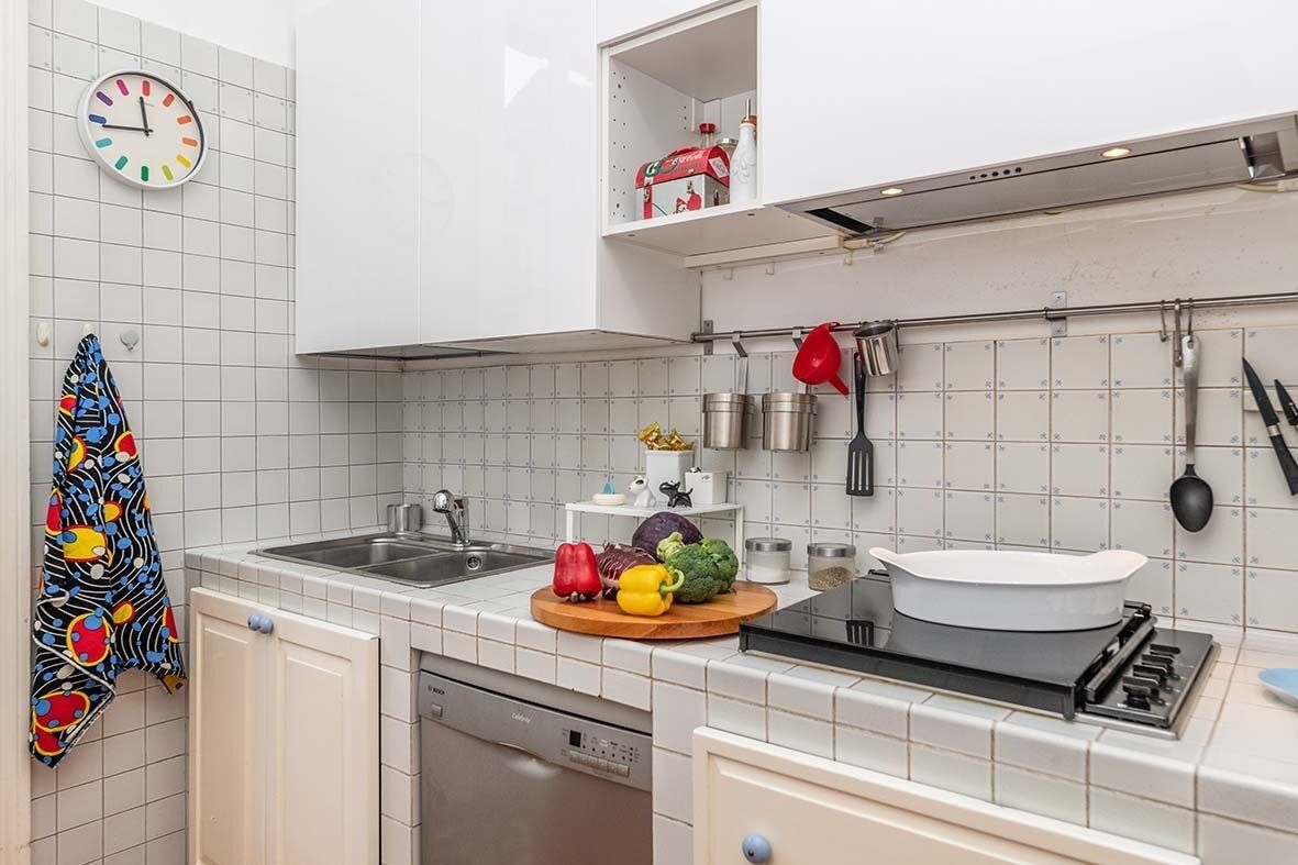 Ett kök med vita skåp, en diskho, en spis och diverse köksredskap.