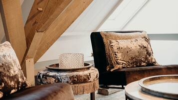 A cozy loft-style room with a sloped ceiling, a cushioned sofa with a patterned throw pillow, a round coffee table, and a small side table with a decorative item.