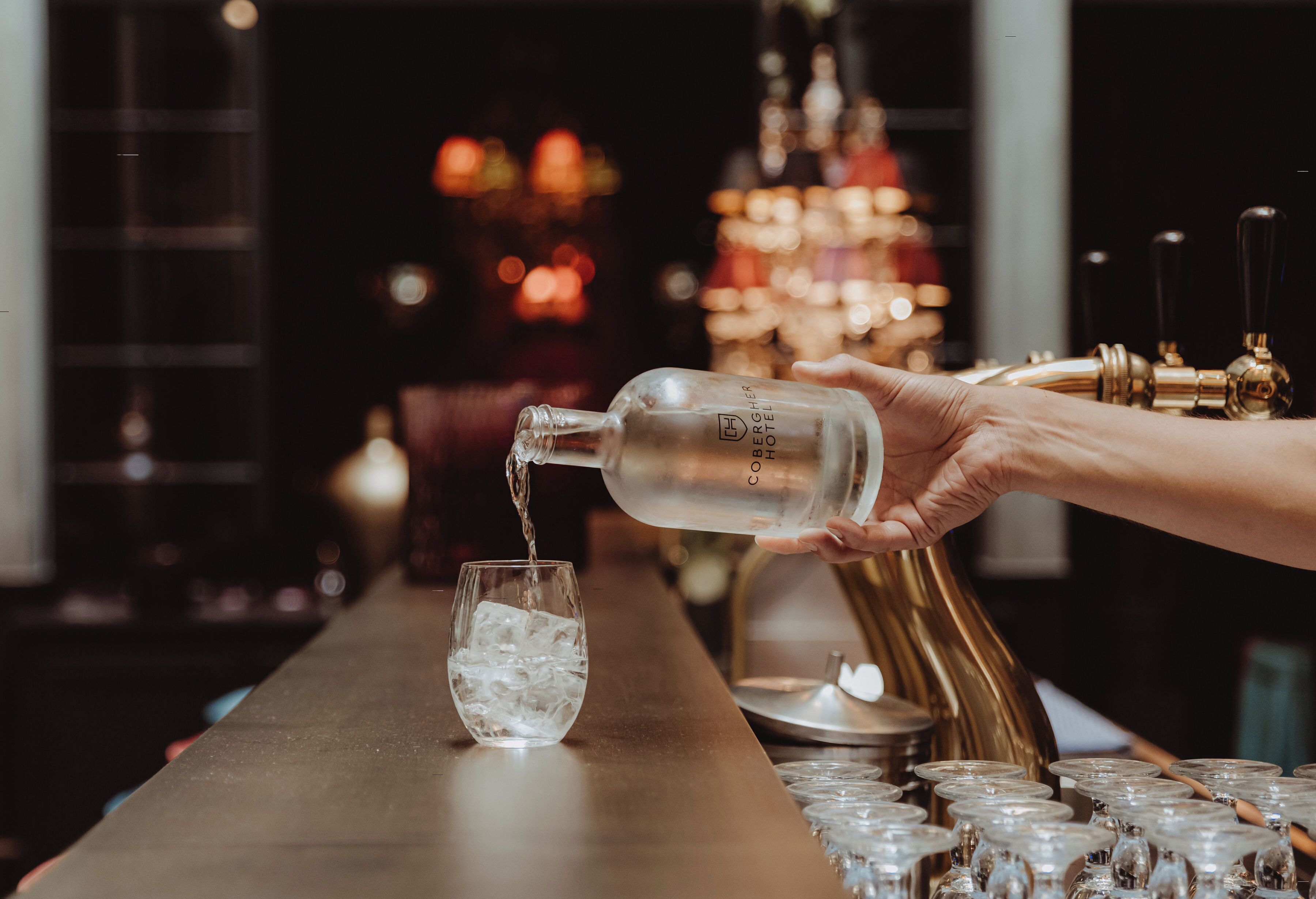 Eine Hand gießt eine klare Flüssigkeit aus einer Flasche in ein Glas mit Eiswürfeln.