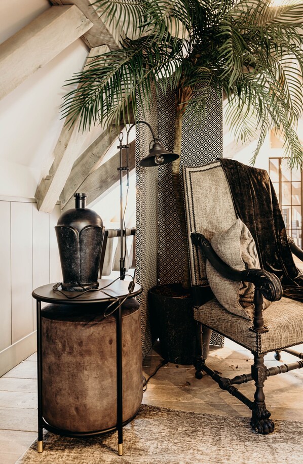 A cozy room with a rustic chair, a small round table, and a large potted plant. - Cobergher Hotel (Kortrijk)