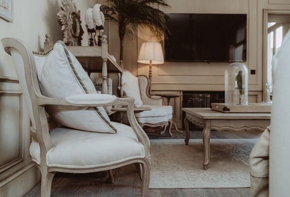 A traditional living room with a classic armchair, a small table, and a television mounted on the wall. - Cobergher Hotel (Kortrijk)