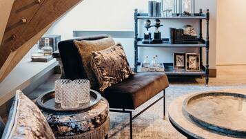 Un espacio tipo loft con vigas de madera a la vista, un sofá de cuero, una mesa de centro redonda y una estantería con marcos y objetos decorativos.