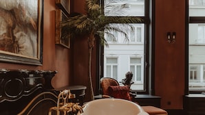 Una habitación con bañera, un ventanal grande, una planta y una estatua.