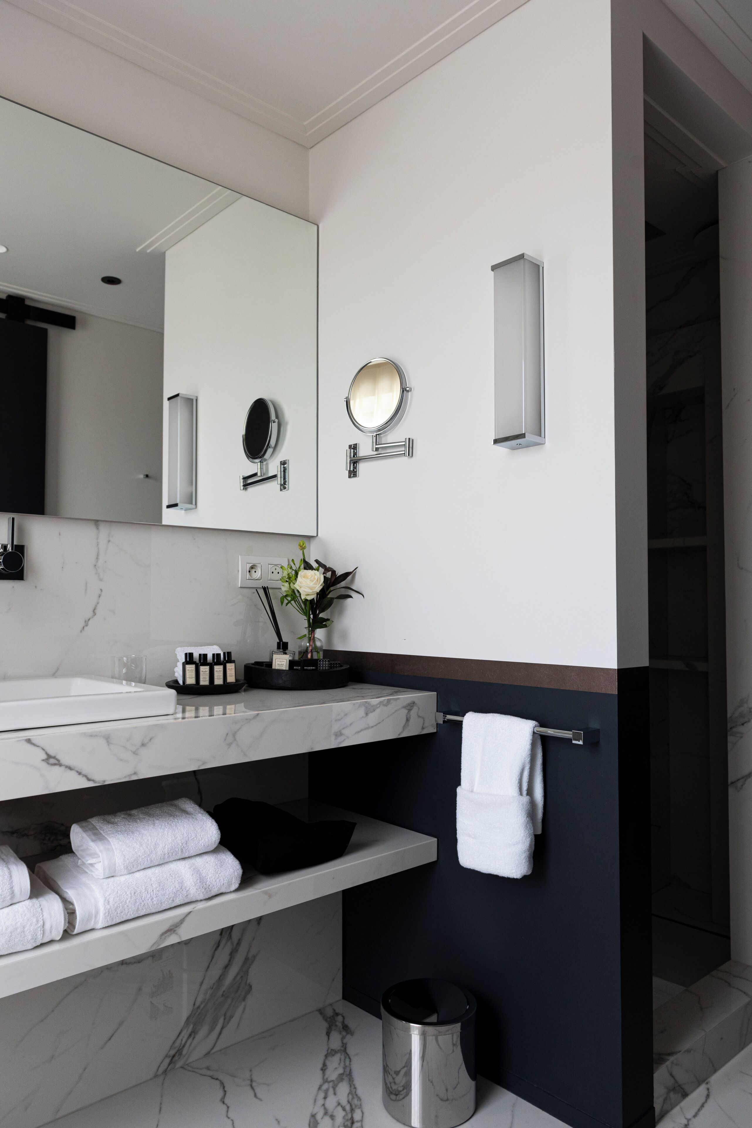 Un baño moderno con encimera de mármol, un espejo grande, un perchero y un cubo de basura pequeño.