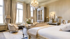 Un dormitorio clásico y elegantemente decorado, con una cama grande, un sillón tipo chaise, una bañera antigua y un candelabro.