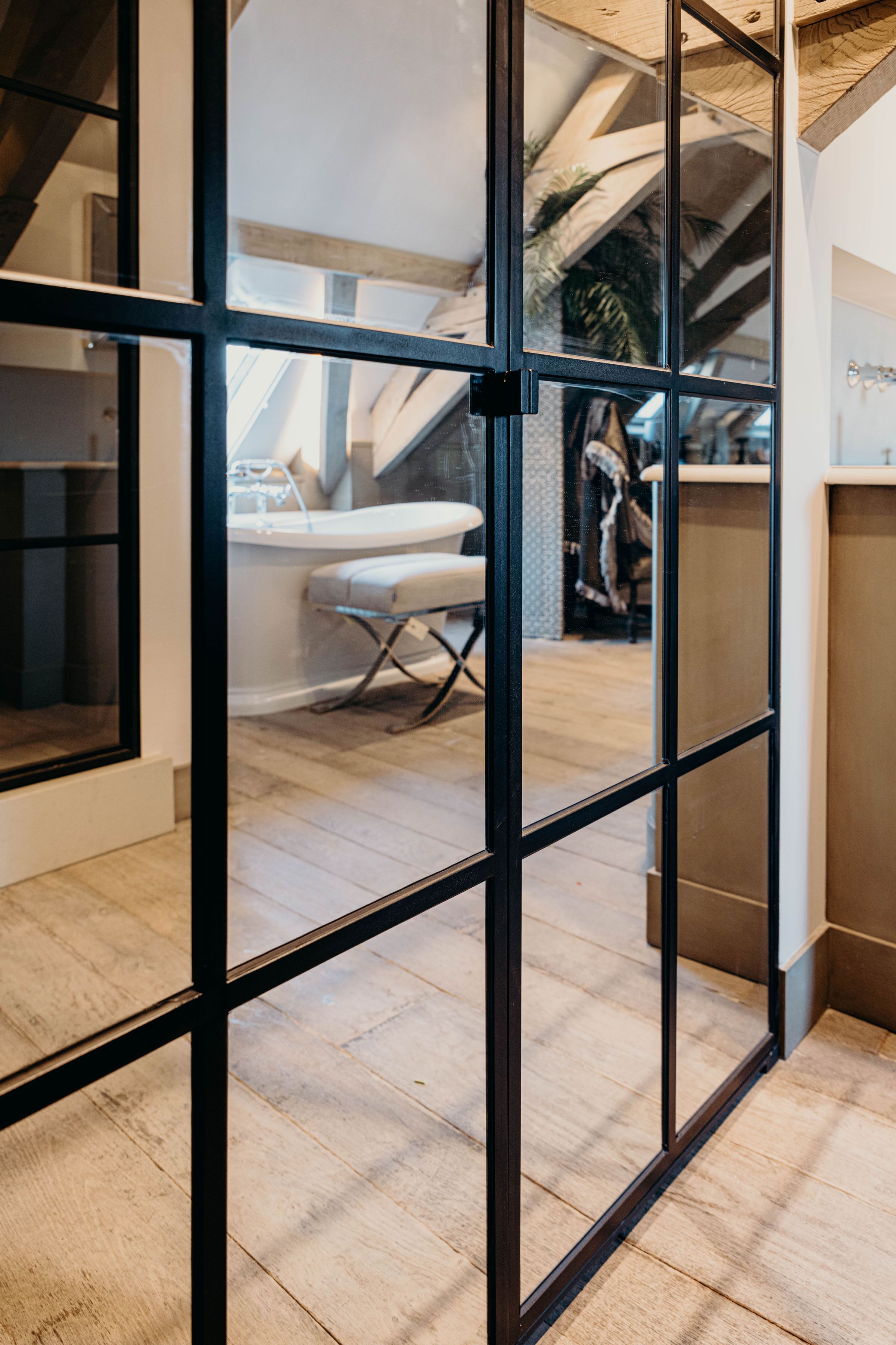 Un interior moderno con piso de madera, una pared divisoria de vidrio y una escalera visible que conduce a un nivel superior.