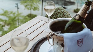 Una mesa con una botella de champán, una copa de vino y un adorno, con vista a un canal y edificios al fondo.