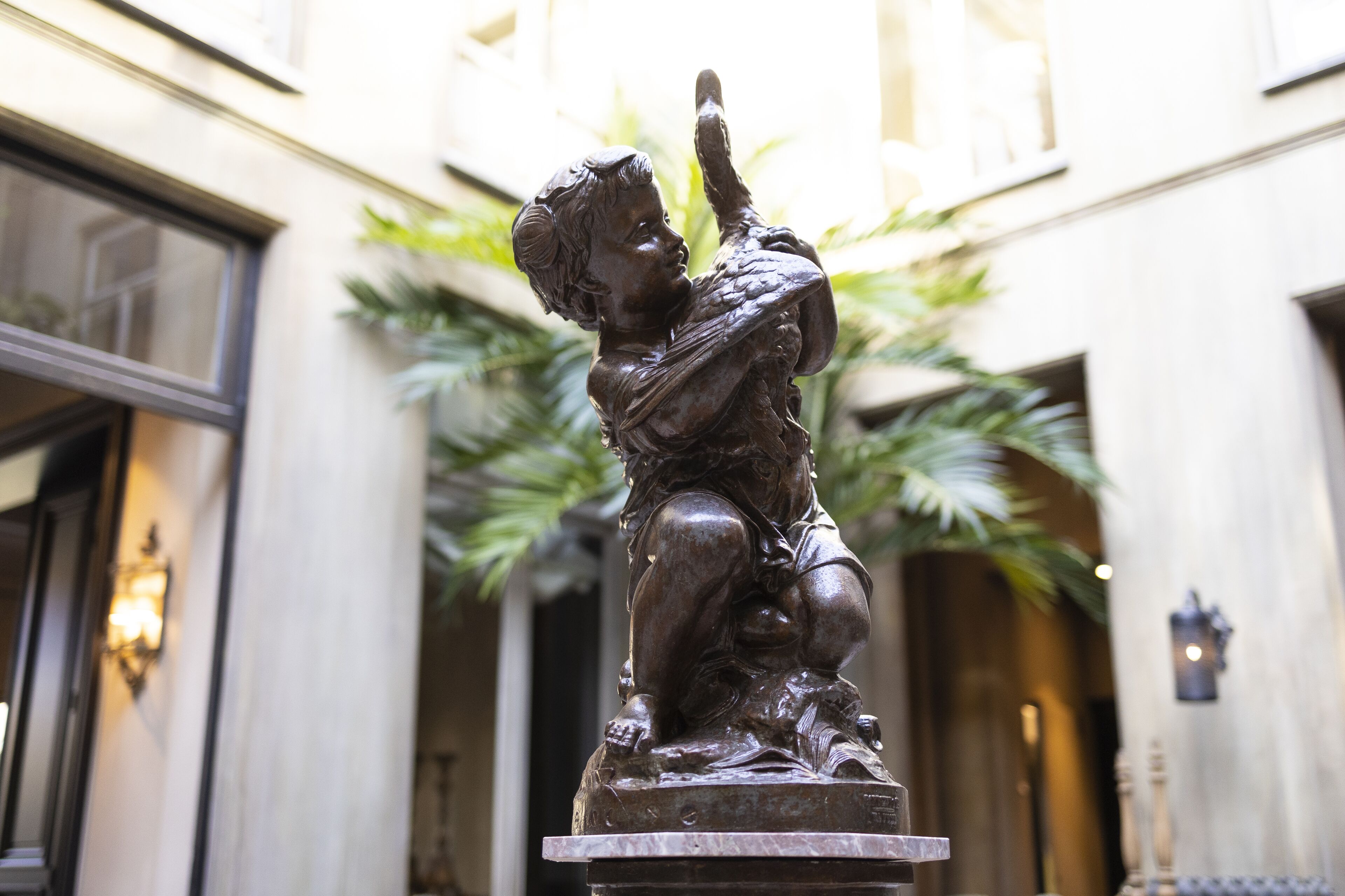 Une statue en bronze représentant un enfant, située dans une cour, avec un bâtiment en arrière-plan.