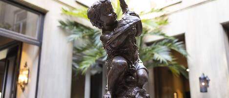 Eine Bronzestatue eines Kindes in einem Innenhof mit einem Gebäude im Hintergrund.