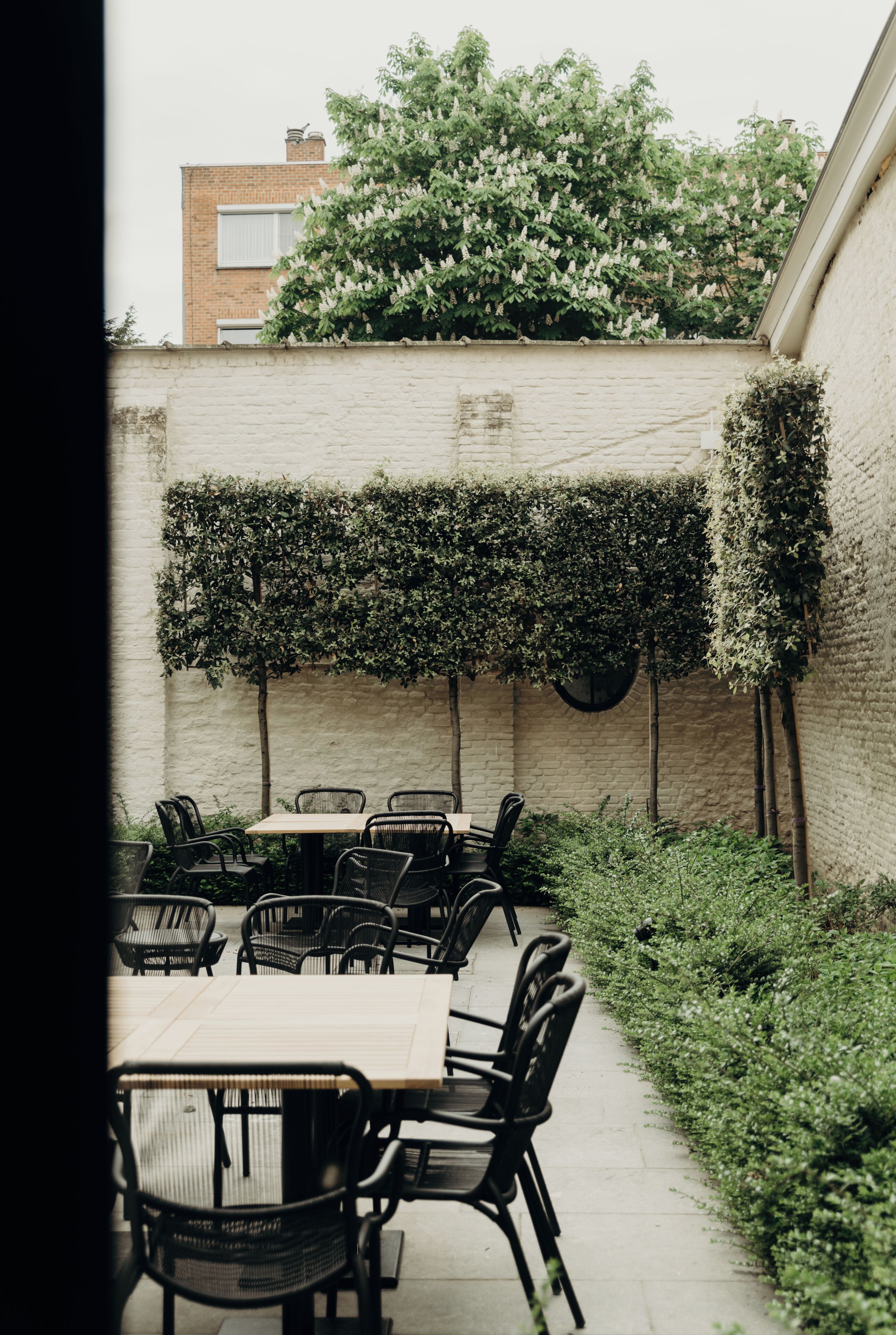 An outdoor seating area with tables and chairs, surrounded by a brick wall and greenery.