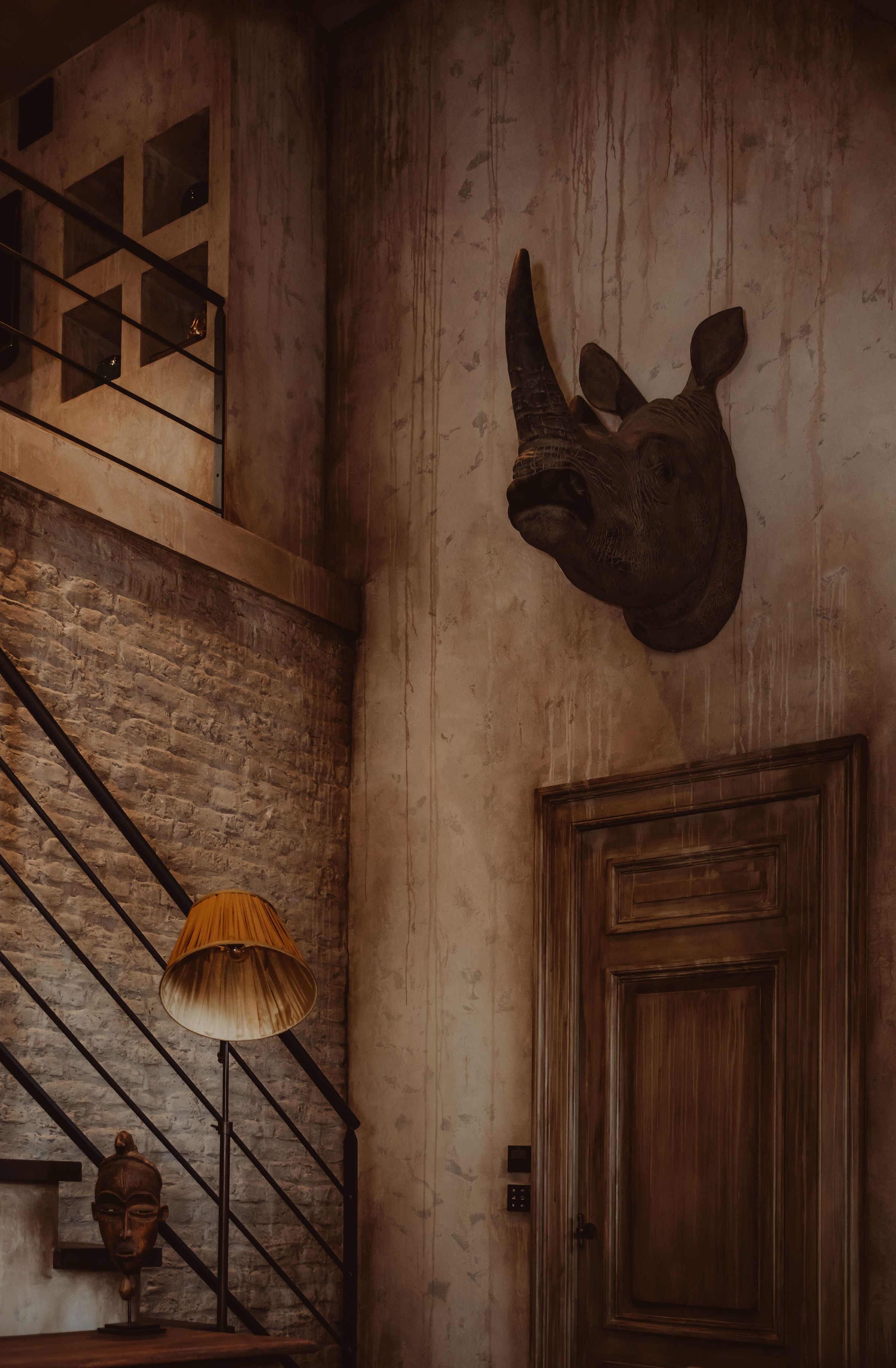 Un escalier avec une rampe en bois, une lampe fixée au mur et une porte dotée d’un panneau en bois.
