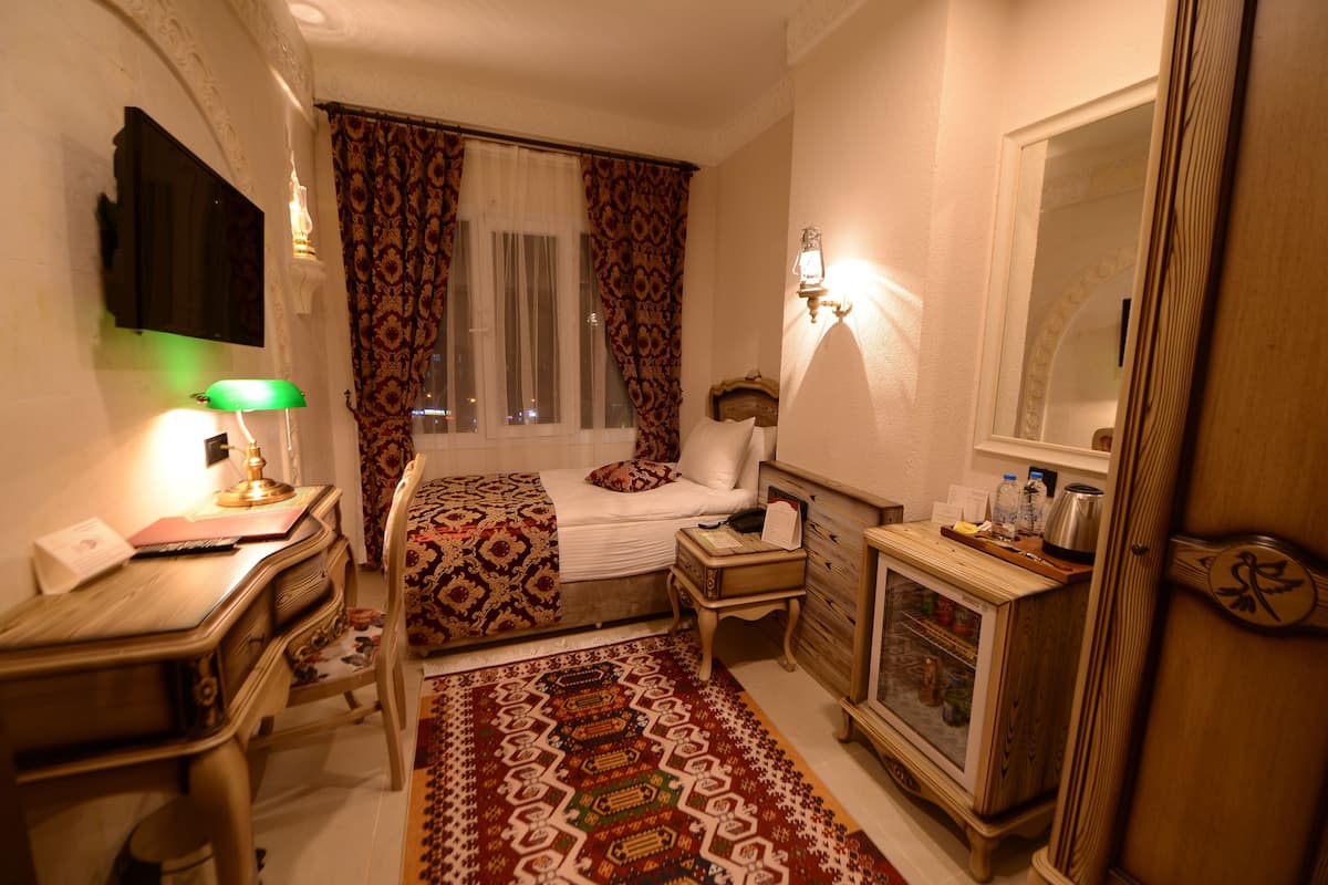 A hotel room with a bed, desk, lamp, nightstand, dresser, and a window with curtains.