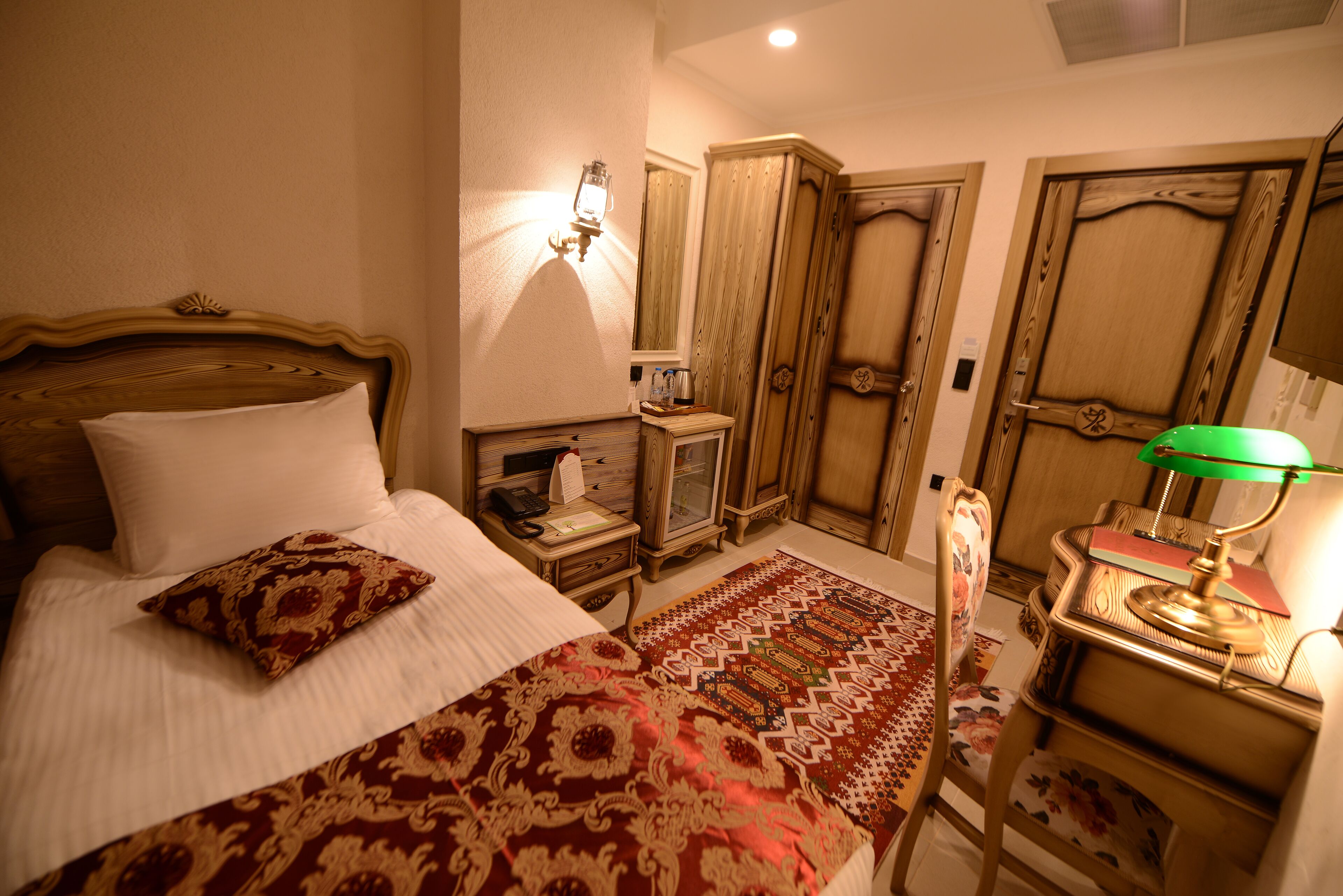 Una habitación tradicional con una cama de madera, un escritorio con lámpara, un espejo y un armario.