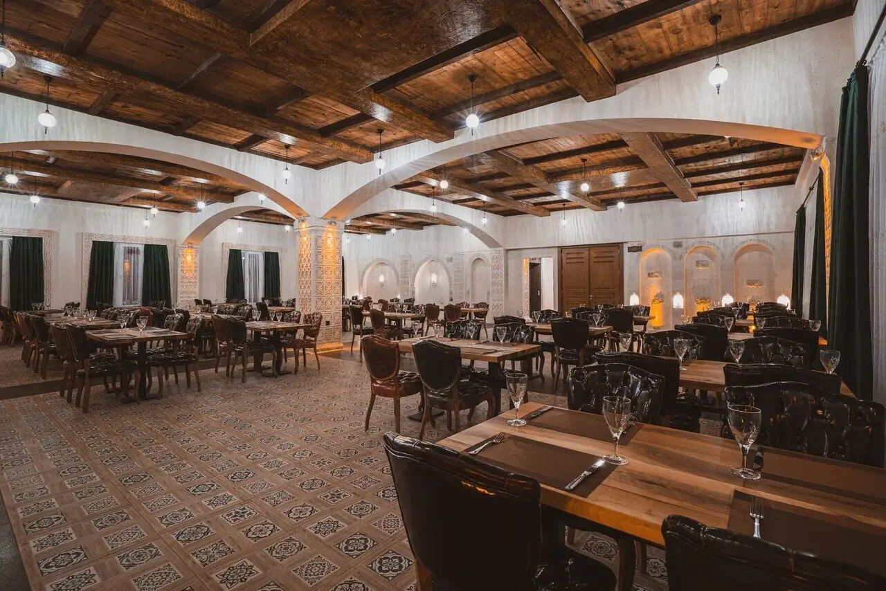 Uma sala de jantar ampla, com altos tetos de madeira e várias mesas e cadeiras.