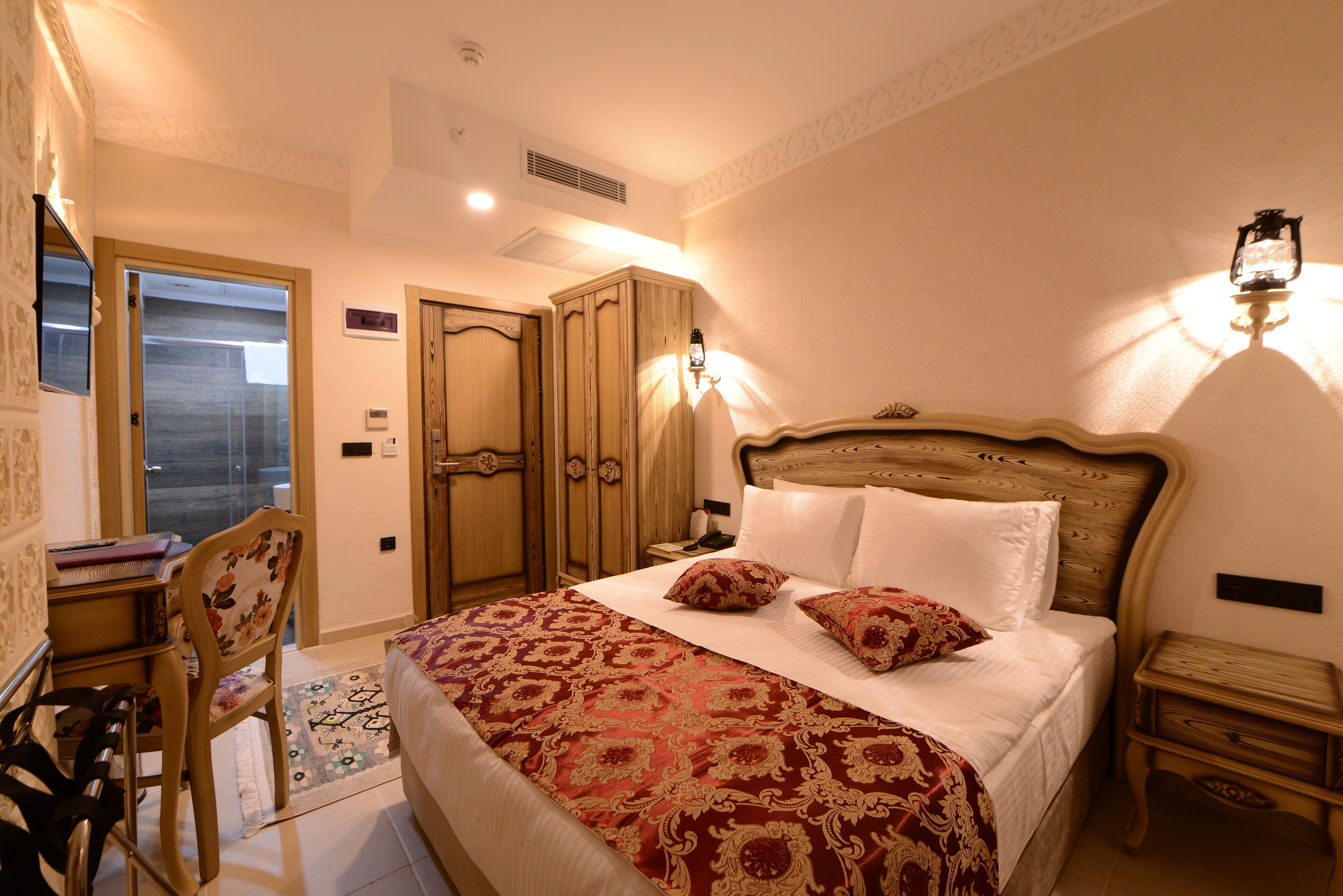 A bedroom with a large bed, a desk with a chair, a wardrobe, and a nightstand.